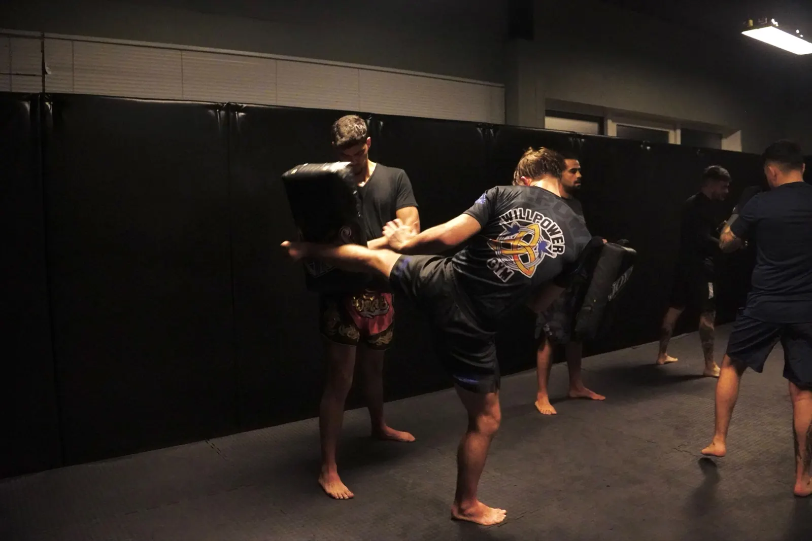 Lid in een Willpower-shirt trapt op een pad dat een trainingspartner vasthoudt